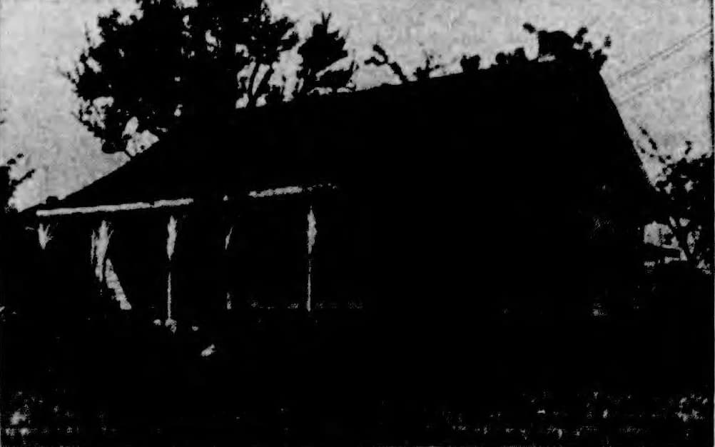 A dark 1949 newspaper photograph of the Old Tod Home on Heron Street, its low roof and porch posts in silhouette against a pale sky